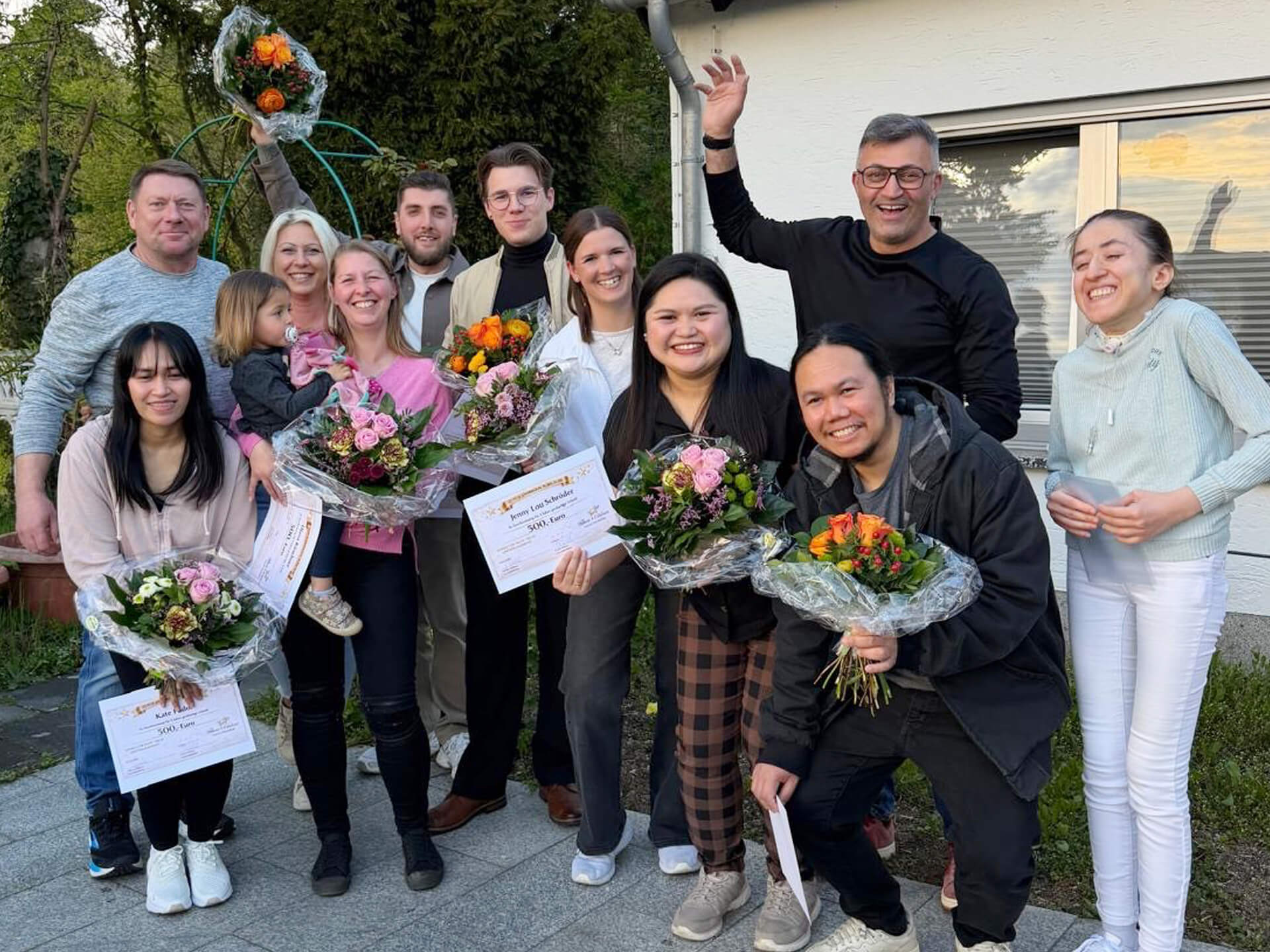 Eine fröhliche Gruppe von Menschen feiert ein Jubiläum in einer Außerklinklichen Wohngemeinschaft und hält Blumensträuße.